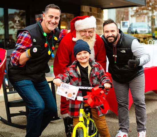 Dr. Ryan Molli, founder of Whole Health Orthopedic Institute & Travis Buzzell, owner of Orthopaedic Solutions, and Santa giving Jaxon a bike.